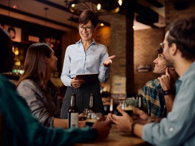 Happy waitress talking to group of guests in a bar.